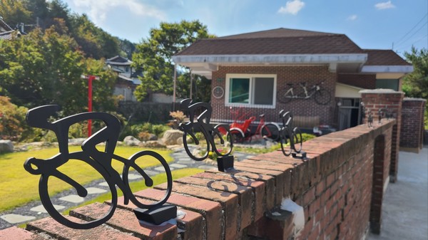 담장에는 자전거 조형물을 장식해 놓았고 뒤쪽에 보이는 집 외벽에도 다양한 자전거가 걸려 있다   
